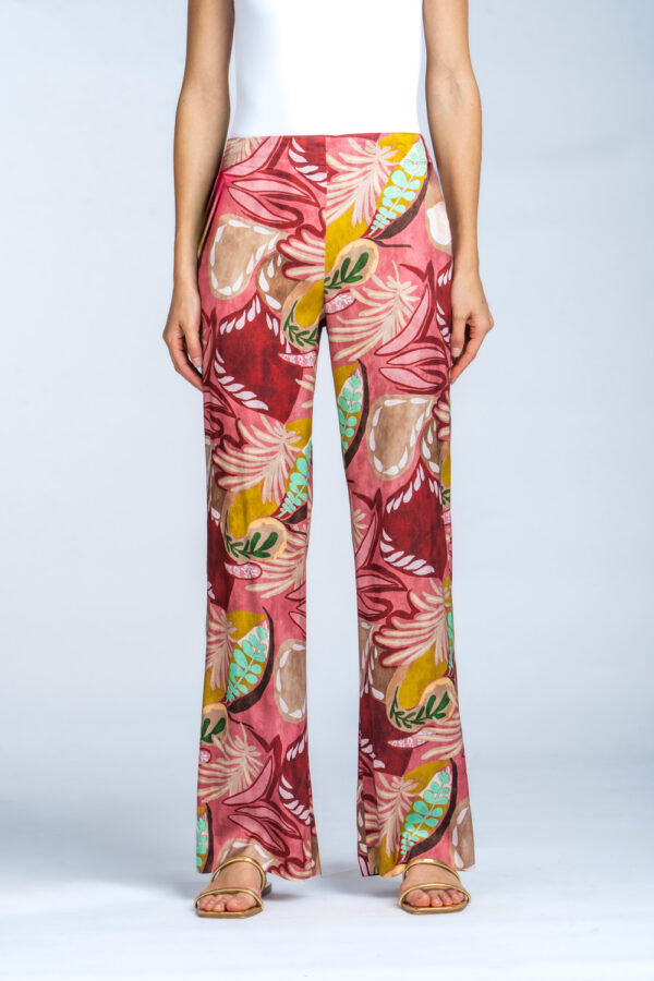 L'inquadratura inferiore di una modella che indossa pantaloni a gamba dritta in raso con una stampa vivace di foglie e motivi astratti in rosa, rosso, giallo, beige e verde, di Via Masini 80, abbinati a sandali dorati.