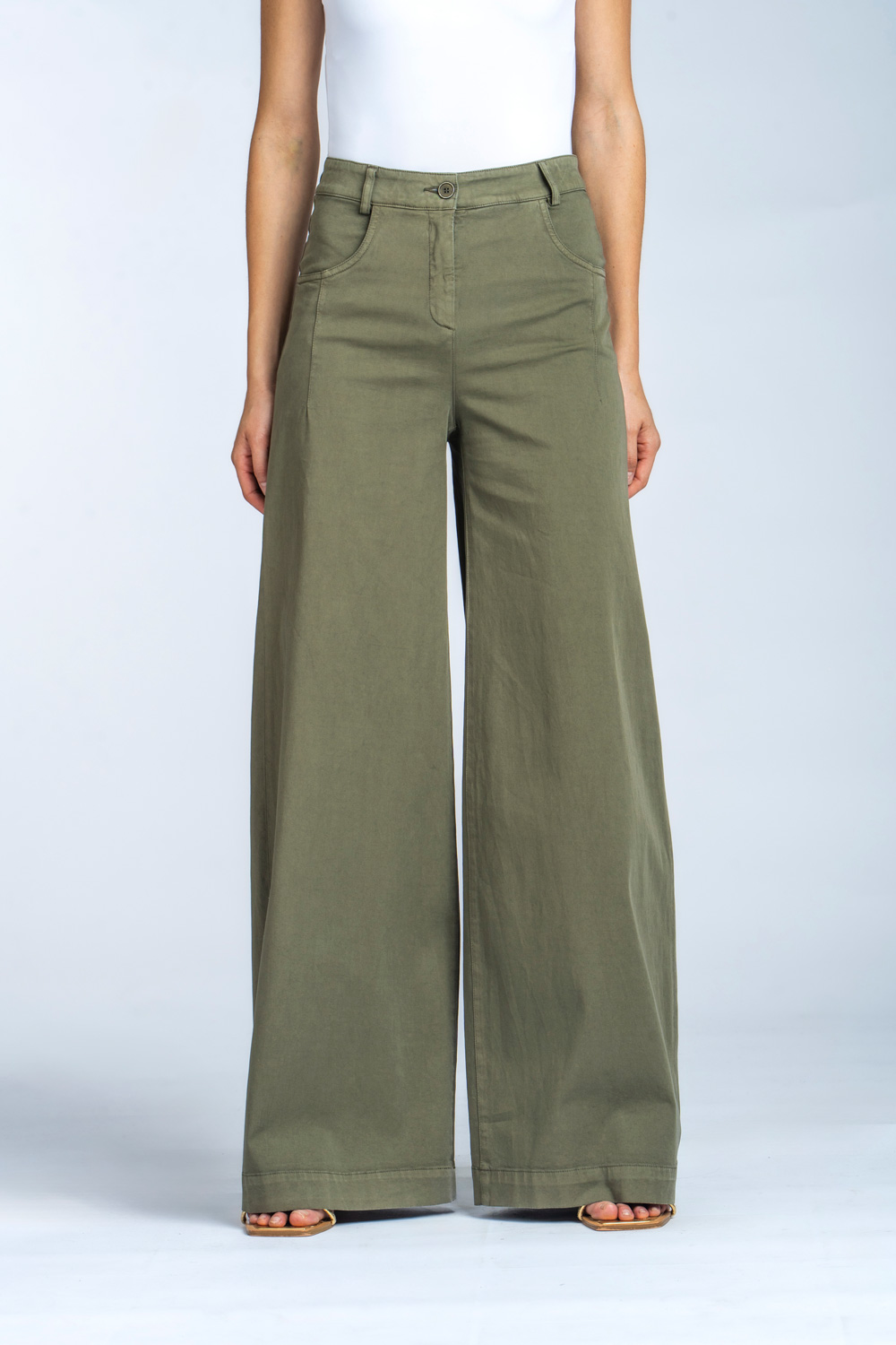L'inquadratura inferiore di una modella che indossa pantaloni larghi a gamba larga in twill di cotone verde oliva di Via Masini 80, con tasche frontali e passanti per cintura, abbinati a sandali dorati.